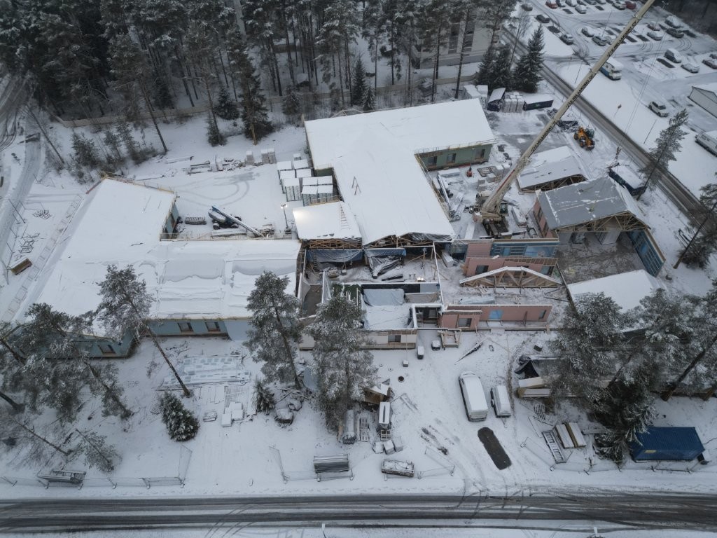 Ilmakuva Mainiokoti Koivunkajon työmaalta, rakennuksen lumisia kattoja ja metsää