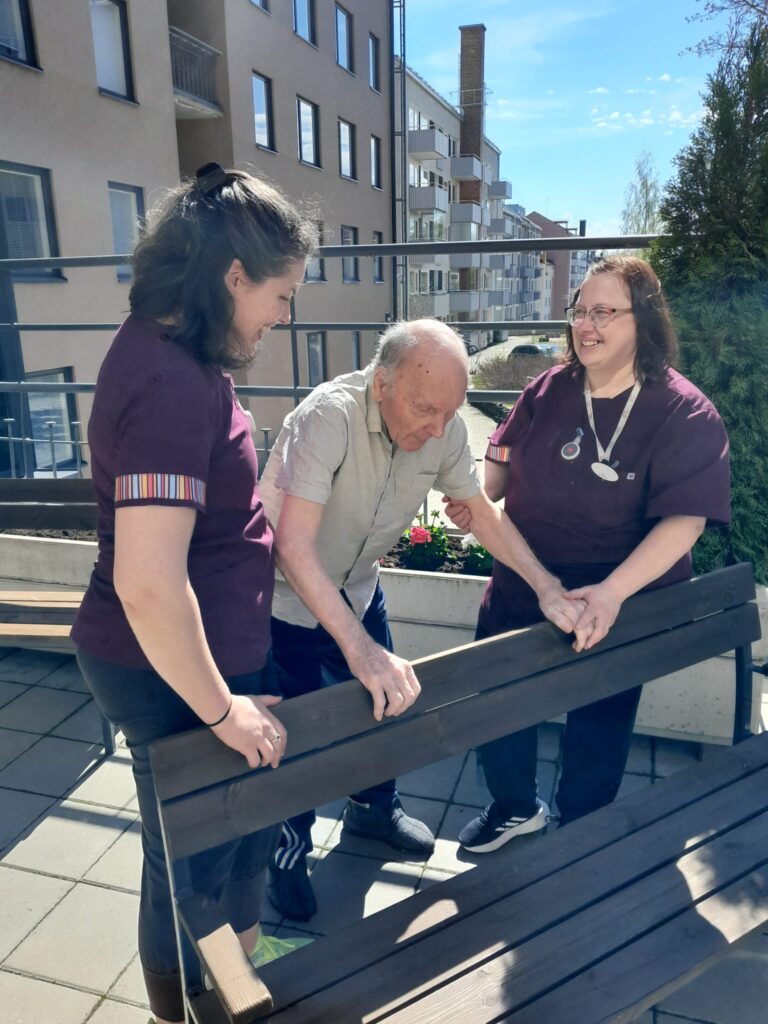 Fysioterapeutti Leonoor ja tiimivastaava Marjo toteuttavat yhdessä asukkaan kuntoutusta ja ulkoilua Mainiokoti Tauluhovin sisäpihalla