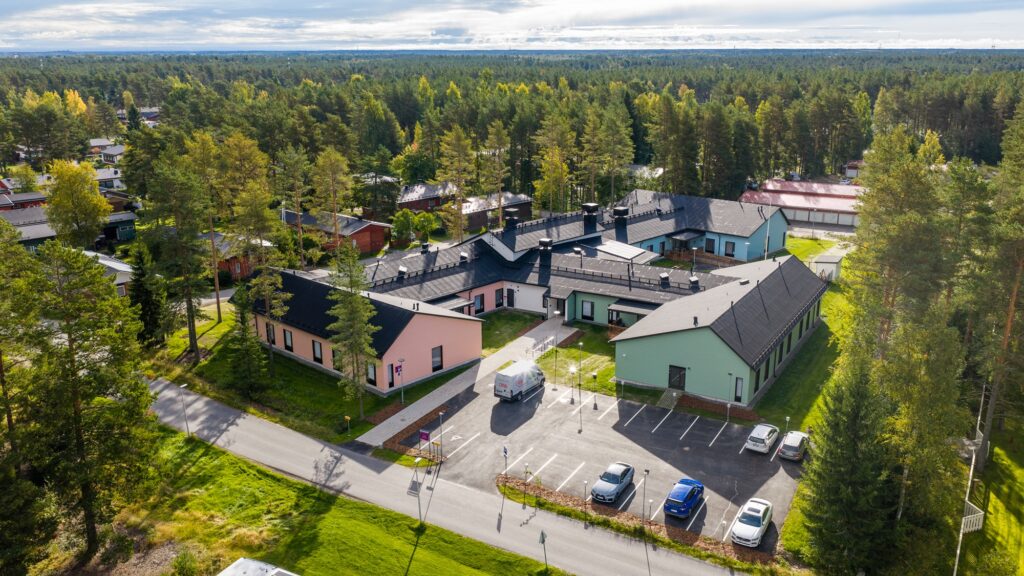 Ilmakuva, jossa rakennus, piha-alue ja ympäröivää metsää.