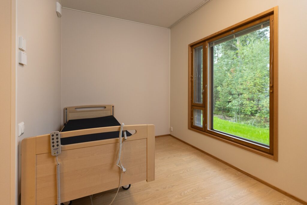 Asuinhuone, jossa on sänky ja suuri ikkuna metsäiseen maisemaan.