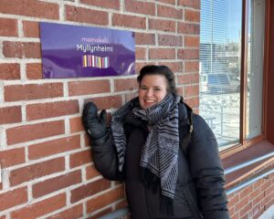 Yksikönjohtaja Veera Kotikivi Mainiokoti Myllynhelmen edessä talvivaatteissa, nimikyltti, jossa lukee Mainiokoti Myllynhelmi