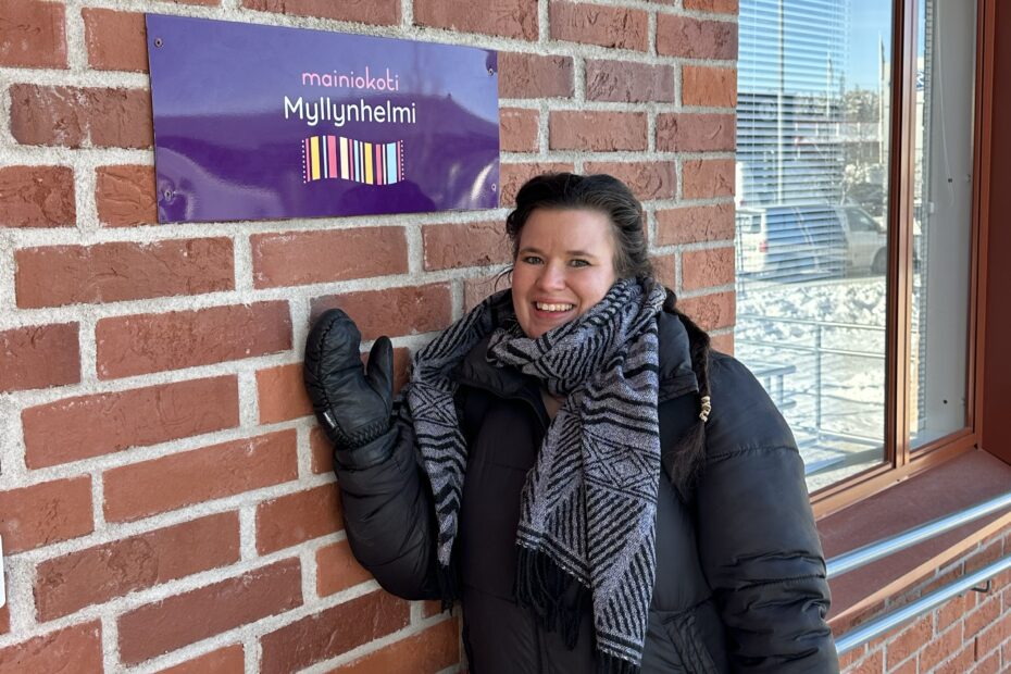 Yksikönjohtaja Veera Kotikivi Mainiokoti Myllynhelmen edessä talvivaatteissa, nimikyltti, jossa lukee Mainiokoti Myllynhelmi