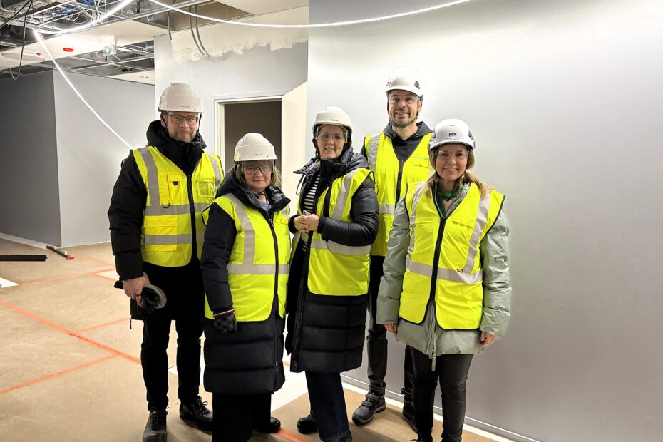 Mainiokotien johtoryhmä huiomioliiveissä ja suojakypärissä Munkkiniemen kohteen työmaalla