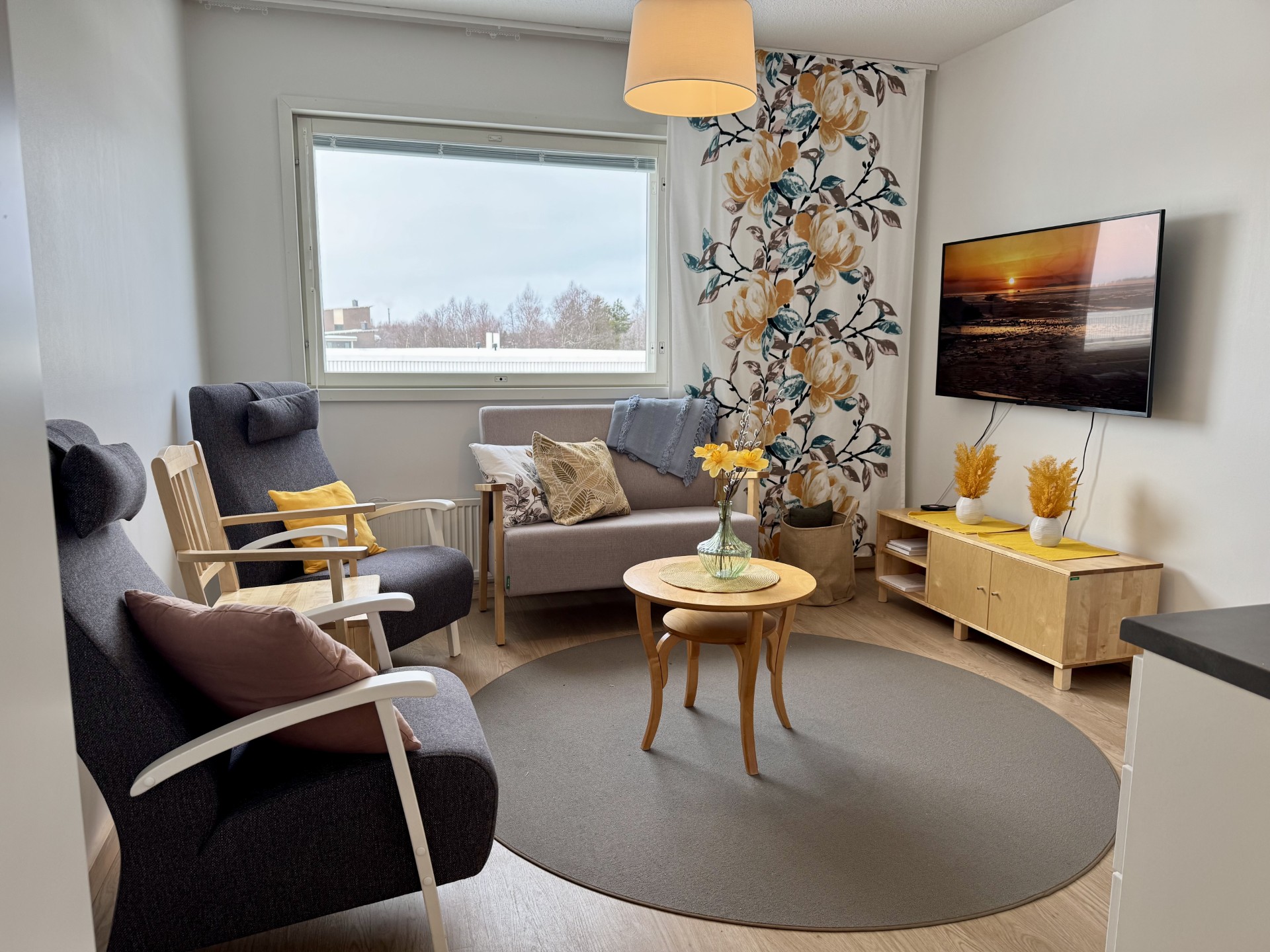 Mainiokoti Rannanhelmen yhteistiloja, nojatuoleja, sohvapöytä keskellä, tv seinällä